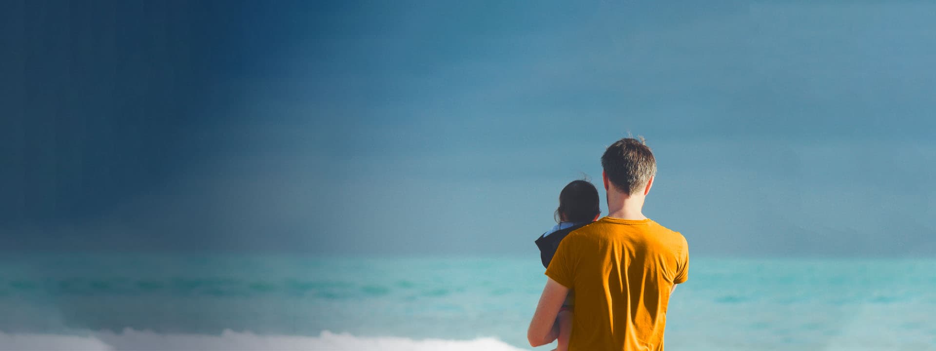 Man holding a child with his back facing the camera looking into the open sky